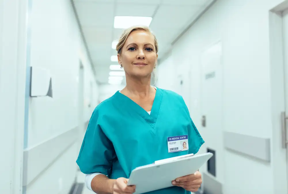 Female nurse in scrubs walking down hallway with chart in hand