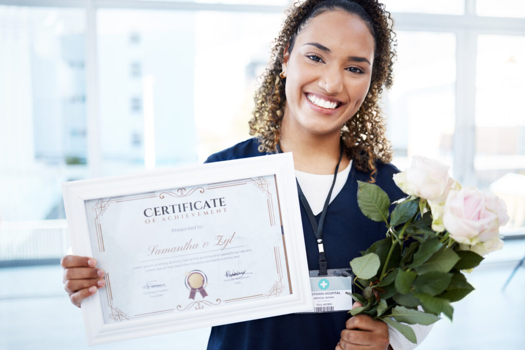 African American nurse holding a certificate of completion and flowers while smiling.