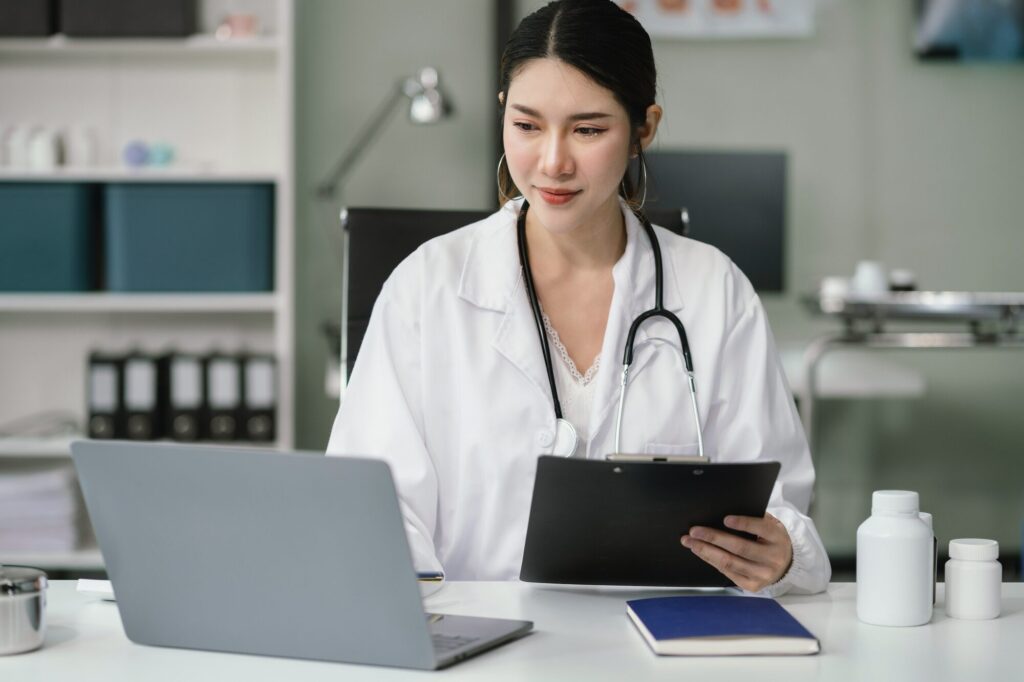 Doctor working on laptop computer and tablet and medical stethoscope on clipboard on desk