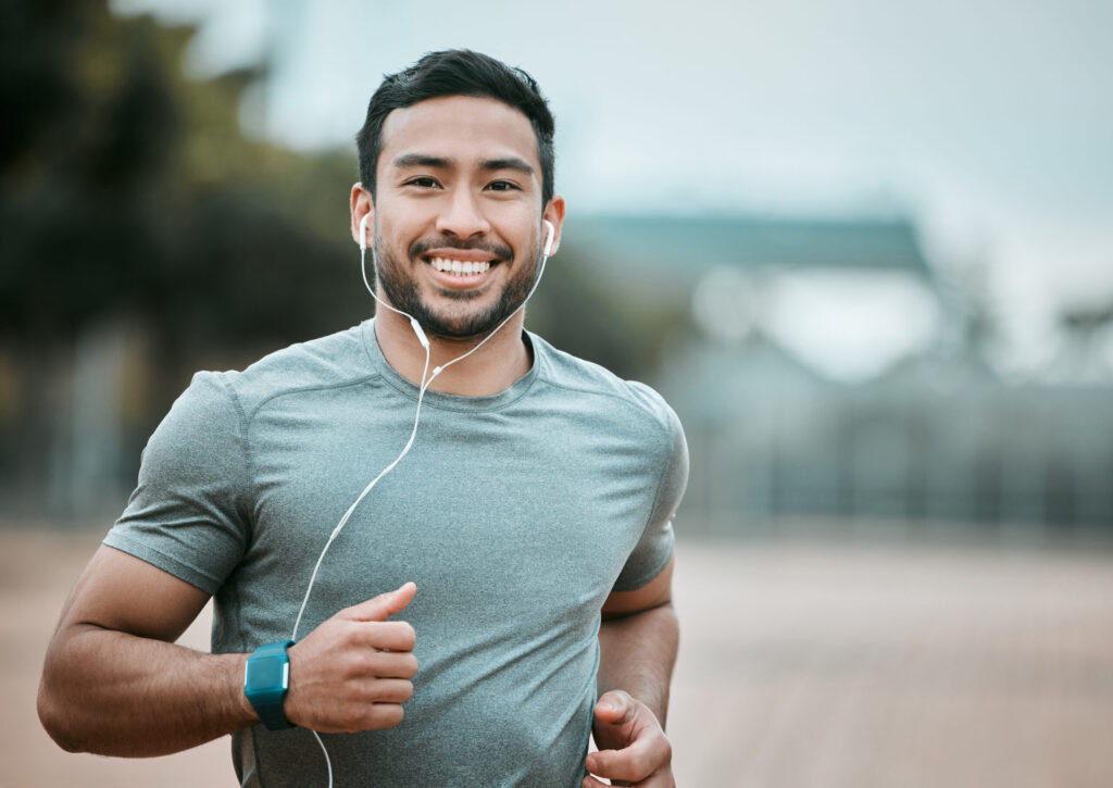 Asian American Male jogging with earbuds, smiling