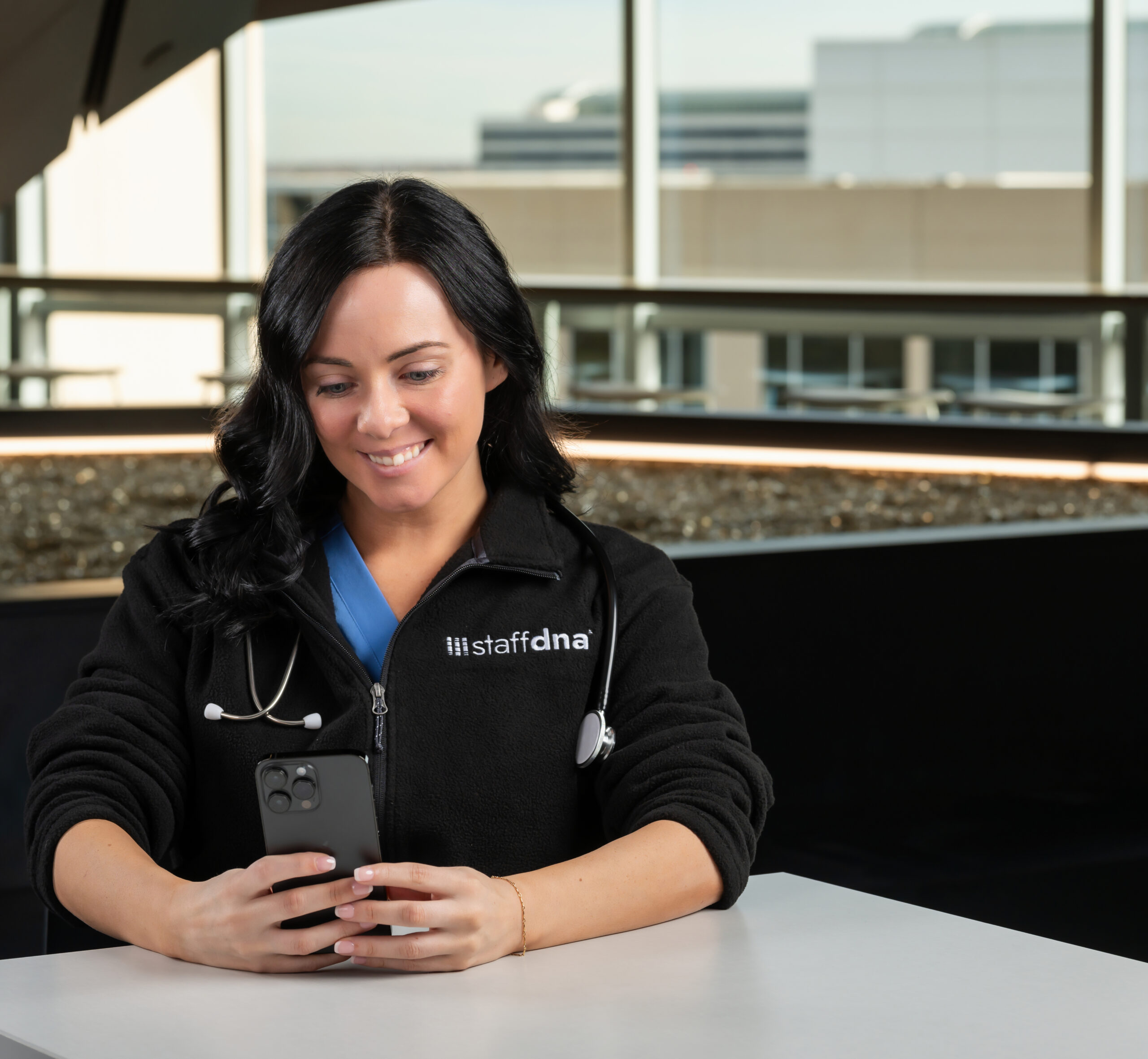 Allied nurse sitting looking at phone and smiling